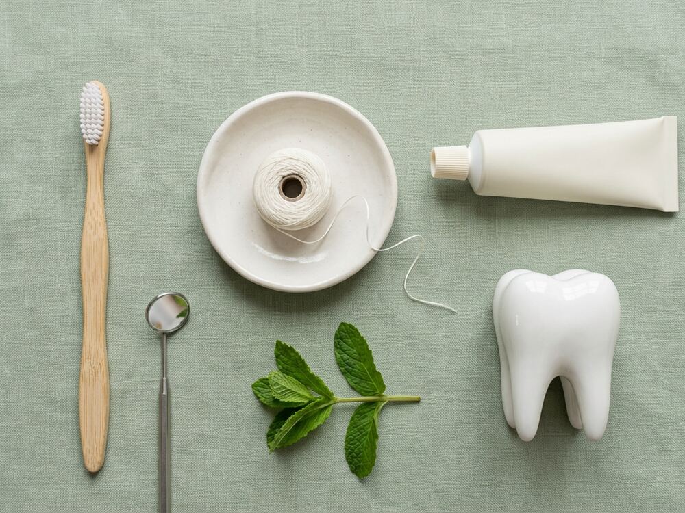 Bamboo toothbrush, floss and a model tooth on a sage surface